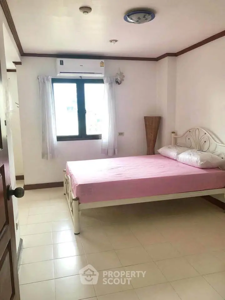 Cozy bedroom with pink bedding and natural light, featuring a simple yet elegant design.