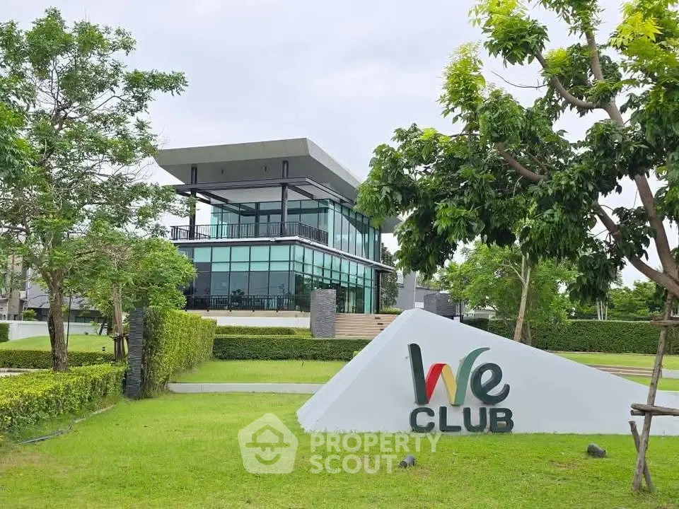 Modern clubhouse with glass facade surrounded by lush greenery and manicured lawns.