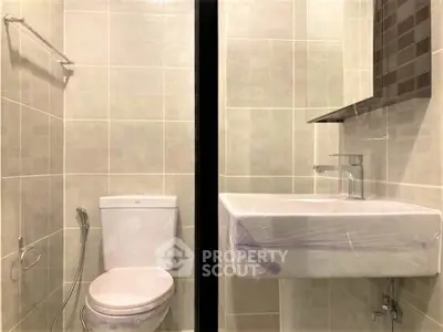 Modern bathroom with sleek fixtures and neutral tiles, featuring a toilet and sink.