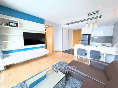 Modern living room with open kitchen, featuring sleek furniture and a large TV, perfect for urban living.