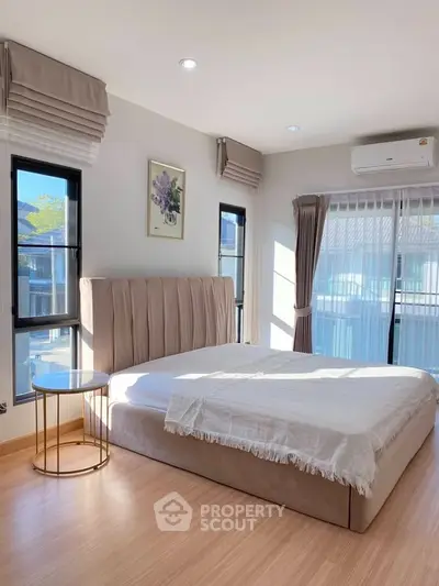 Modern bedroom with elegant decor, large windows, and natural light, featuring a stylish bed and side table.