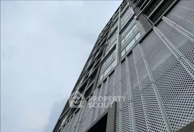 Modern high-rise building with unique perforated metal facade and large windows.