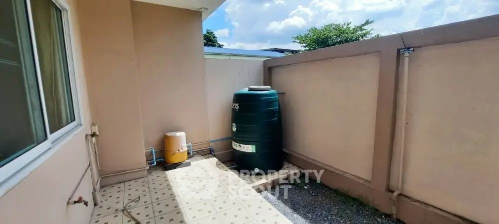 Outdoor utility area with water tank and tiled flooring in a residential property.