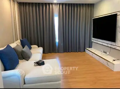 Modern living room with elegant sofa and large TV, featuring stylish curtains and wooden flooring.