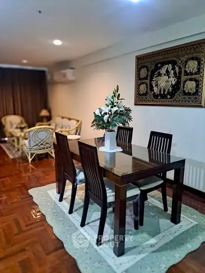 Elegant dining area with wooden table and chairs, featuring a decorative wall art and cozy seating in the background.