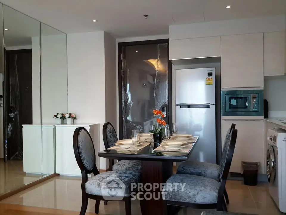 Modern dining area with elegant table setting, mirrored wall, and sleek kitchen appliances in a stylish apartment.