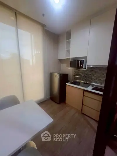 Modern compact kitchen with sleek cabinetry and dining area in cozy apartment.