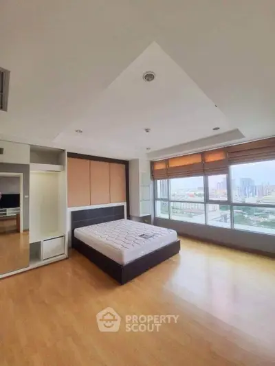 Spacious bedroom with large windows offering a stunning city view, featuring a modern bed and wooden flooring.