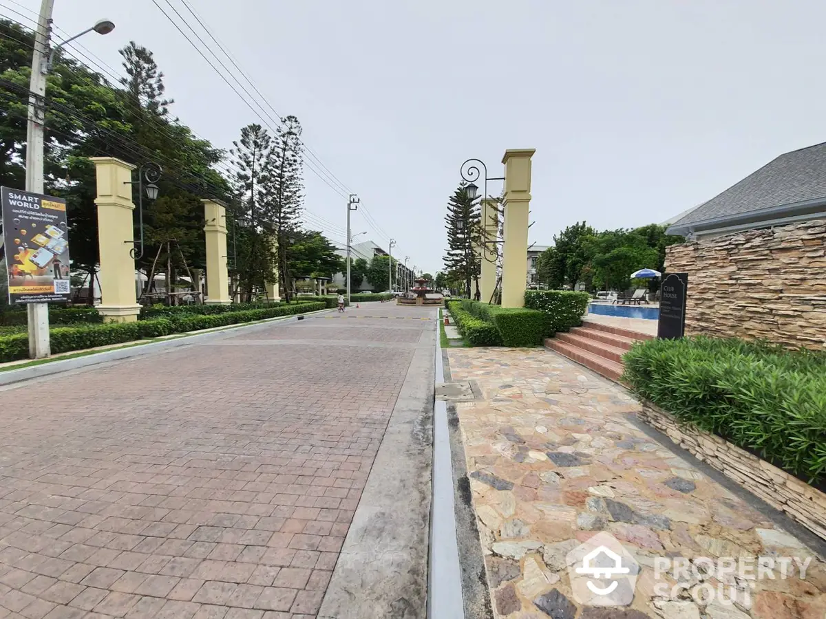 Elegant gated community entrance with manicured lawns, stone-clad pillars, and a welcoming paved driveway leading to luxury homes.