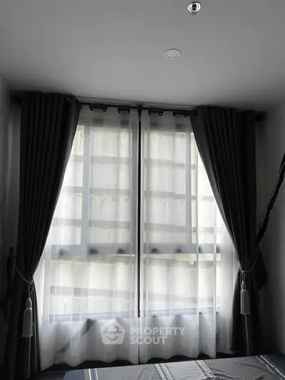 Cozy bedroom with large window and elegant curtains, inviting natural light.