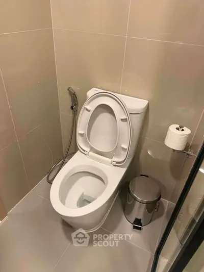 Modern bathroom with sleek toilet and beige tiles, featuring a convenient bidet spray and stainless steel trash bin.