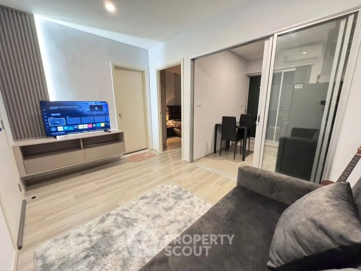 Modern living room with sleek furniture and sliding glass doors leading to a dining area.