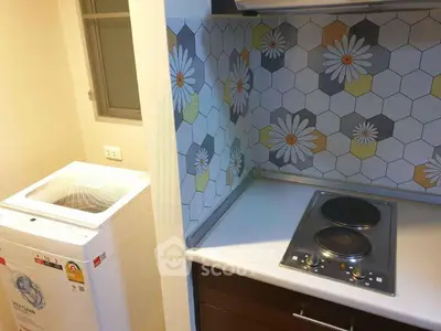 Compact kitchen with electric stove and washing machine, featuring floral hexagonal backsplash tiles.