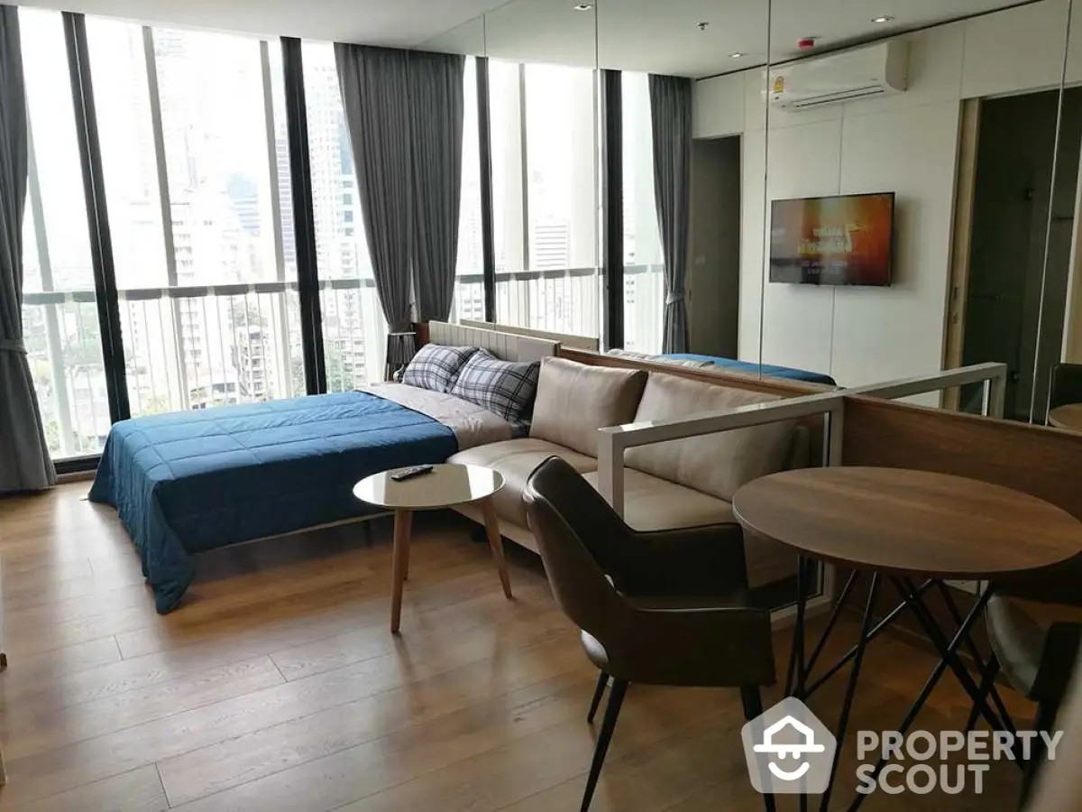 Modern studio apartment with city view, featuring stylish furniture and large windows.