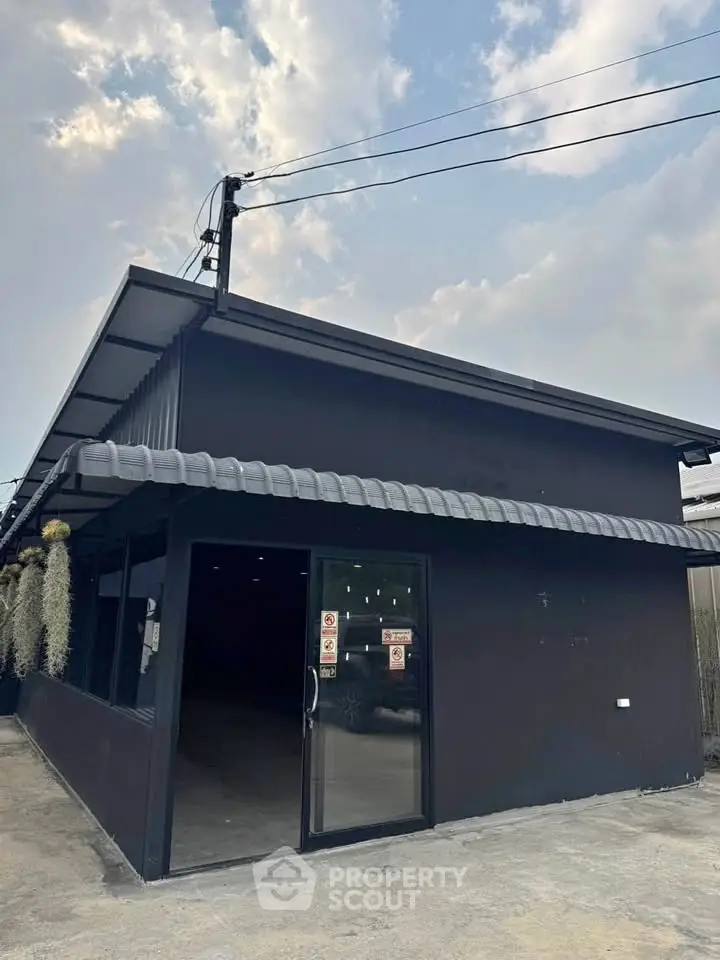 Modern commercial building with sleek black exterior and large glass entrance under a clear sky.