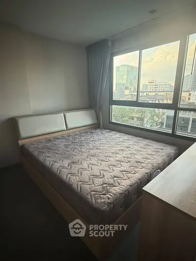 Spacious bedroom with large window offering city views, featuring a modern bed and neutral decor.