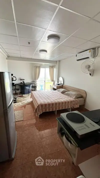 Cozy studio apartment with bed, desk, and kitchenette, featuring a bright window view.