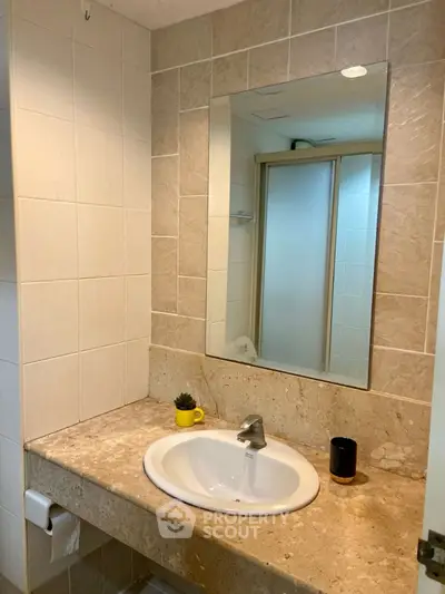 Modern bathroom with elegant sink and large mirror, featuring stylish beige tiles.
