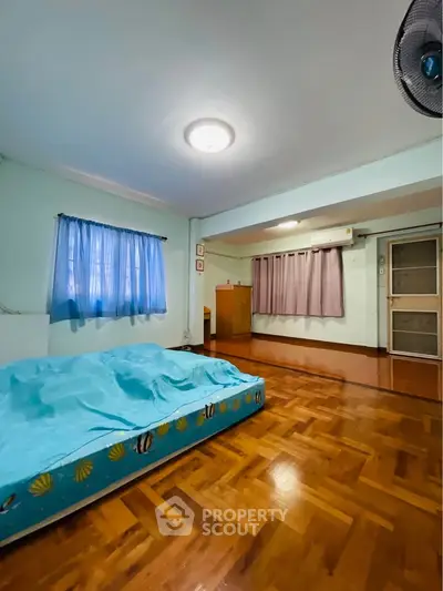 Spacious bedroom with wooden flooring and natural light, featuring a cozy bed and large windows.