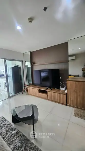 Modern living room with sleek furniture and large TV, featuring a glass coffee table and stylish decor.