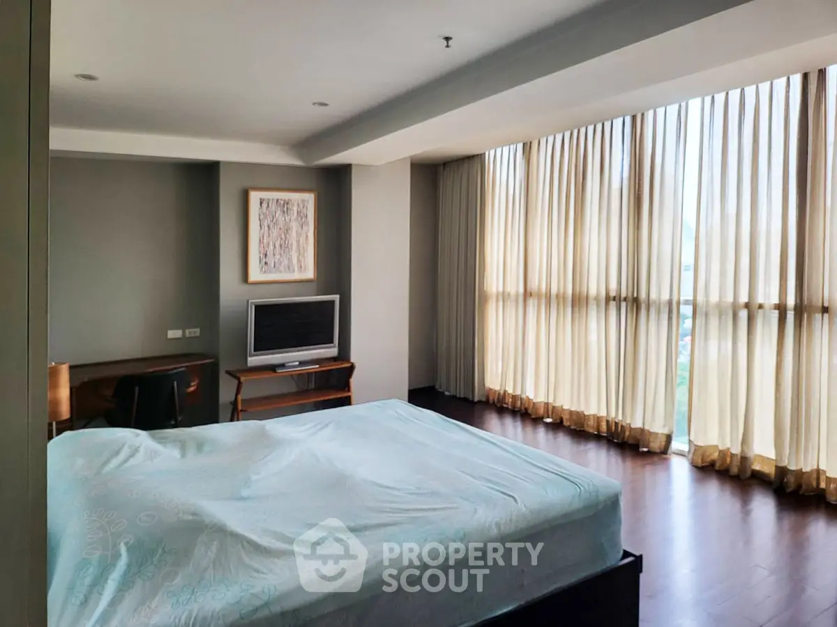 Spacious bedroom with large windows and modern decor in a luxurious apartment.