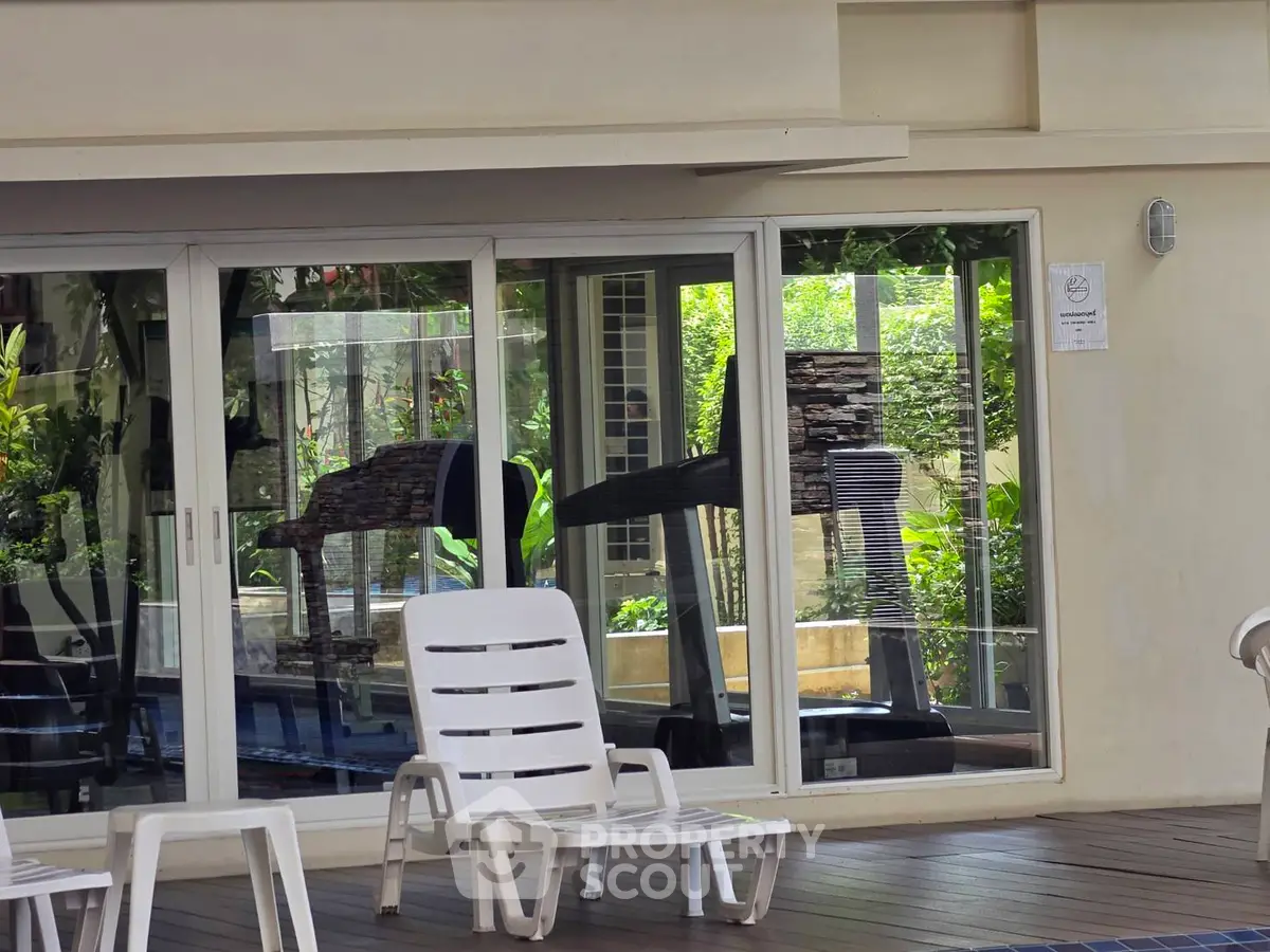Modern gym with glass walls overlooking lush greenery and poolside seating area.