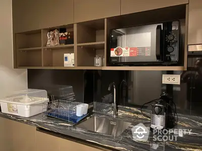 Modern kitchen with sleek cabinetry, microwave, and espresso machine on elegant marble countertop.