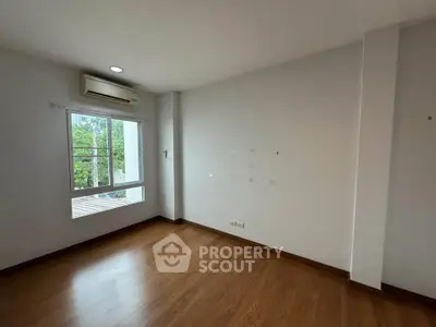 Spacious empty room with wooden flooring and large window, perfect for customization.