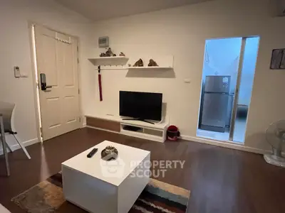 Cozy living room with modern decor and TV unit, adjacent to kitchen area with fridge.