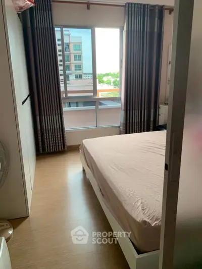 Cozy bedroom with large window offering natural light and city view, perfect for relaxation.