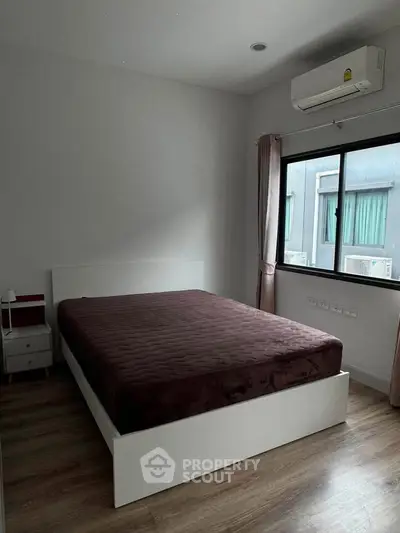 Modern bedroom with large window and air conditioning, featuring a stylish bed and wooden flooring.