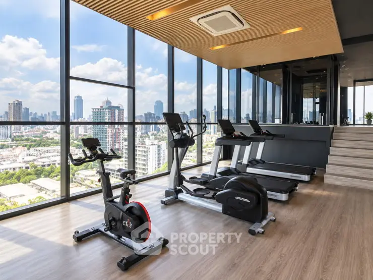 Modern gym with city view, featuring exercise bikes and treadmills in a high-rise building.