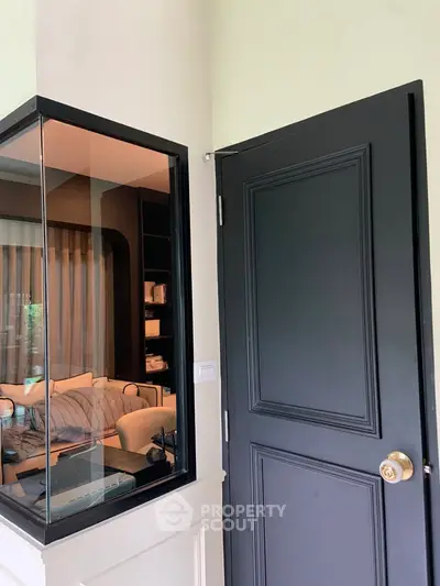 Modern interior with black door and glass partition revealing cozy living room.