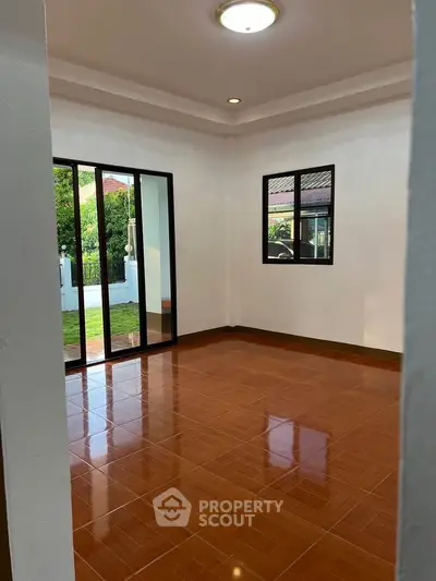 Spacious empty room with glossy wooden flooring and large windows overlooking a garden.