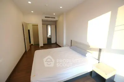 Spacious bedroom with wooden flooring and ample natural light in modern apartment.