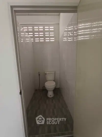 Compact bathroom with tiled walls and floor, featuring a toilet and natural light from a high window.