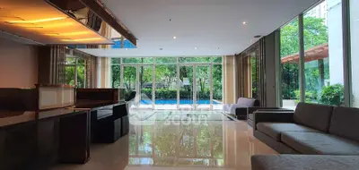 Luxurious living room with floor-to-ceiling windows overlooking a serene pool and lush greenery.