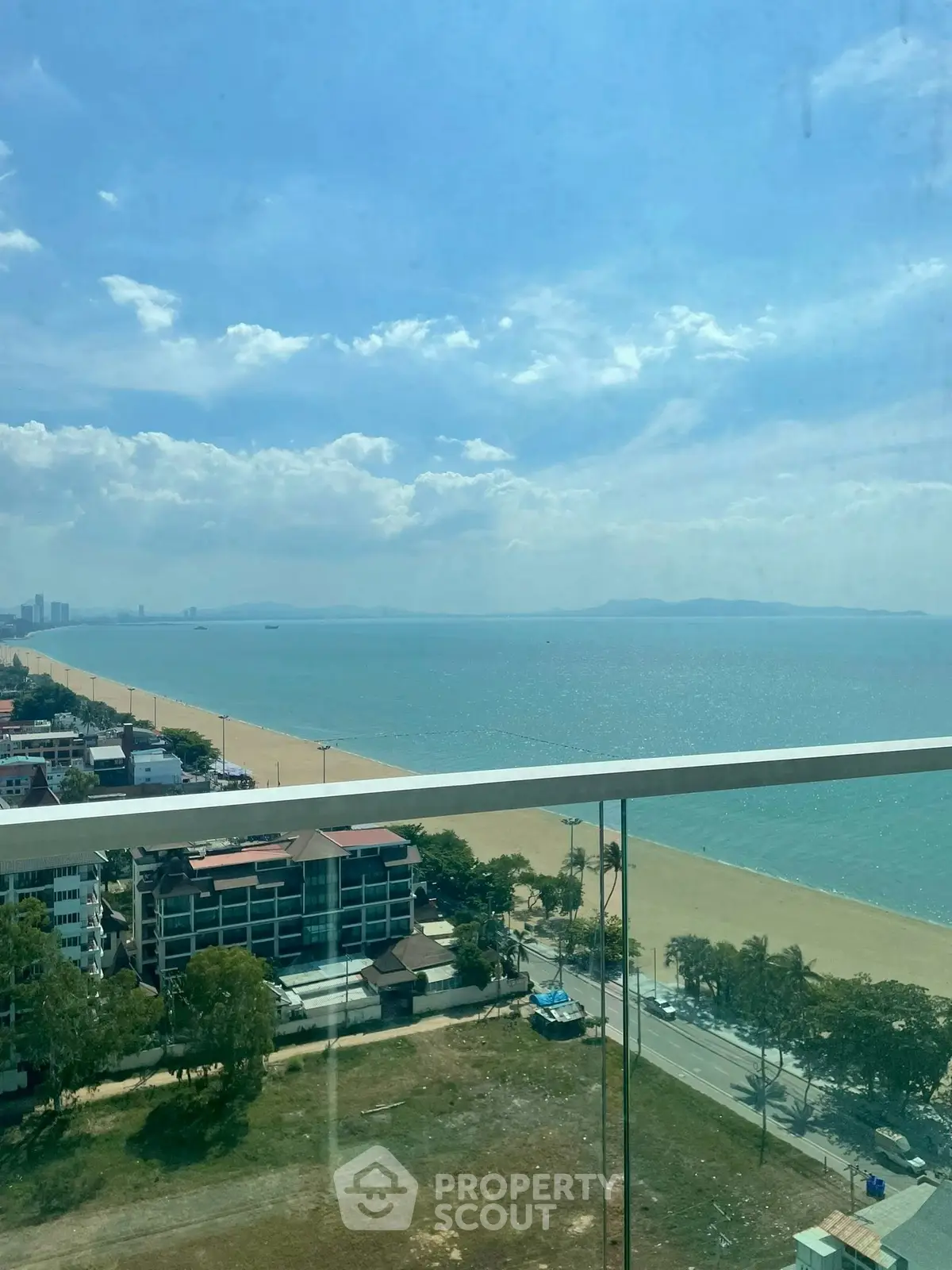 Stunning beachfront view from high-rise balcony with clear blue skies and ocean horizon.