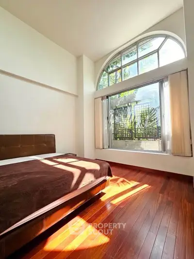 Spacious bedroom with large arched window and hardwood floors