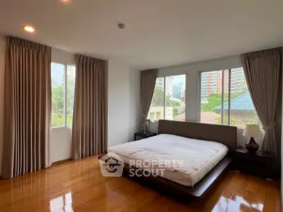 Spacious bedroom with large windows and wooden flooring in a modern apartment.