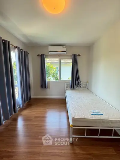 Bright bedroom with single bed, large windows, and air conditioning, featuring elegant wooden flooring.