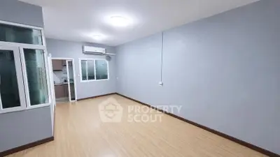 Spacious empty room with wooden flooring and modern kitchen view.