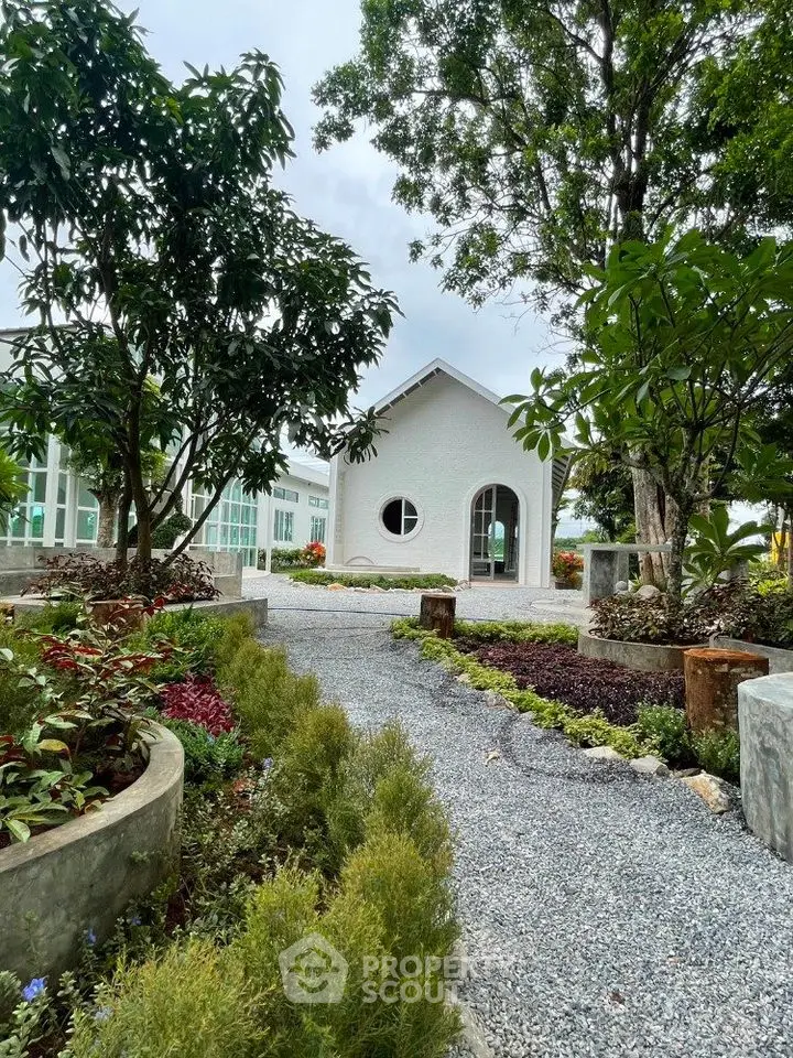 Charming garden pathway leading to a quaint white house surrounded by lush greenery.