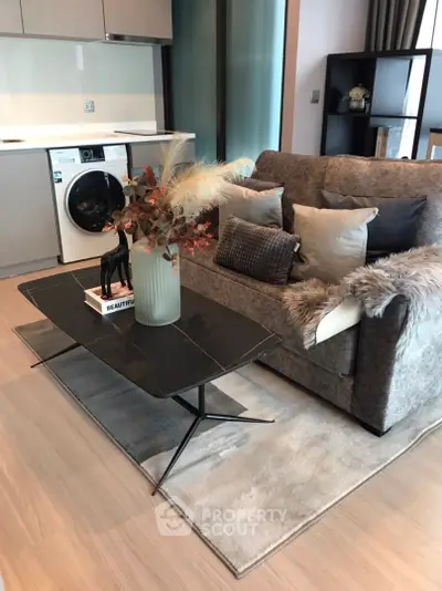 Modern living room with cozy sofa, stylish coffee table, and integrated kitchen with washing machine.
