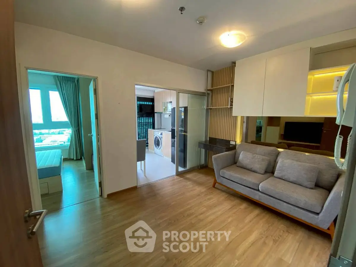 Modern living room with cozy sofa and view into bedroom and kitchen with washing machine.