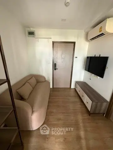 Cozy living room with modern sofa, wall-mounted TV, and wooden flooring in a compact apartment.