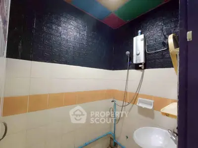 Compact bathroom with modern water heater and tiled walls, ideal for efficient space utilization.