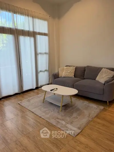 Cozy living room with modern sofa and coffee table, featuring large windows and elegant wooden flooring.