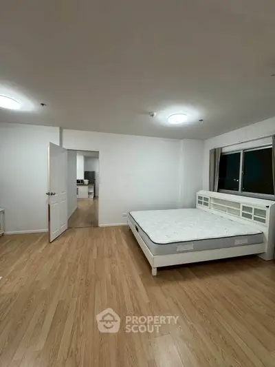 Spacious bedroom with wooden flooring and large window in modern apartment.