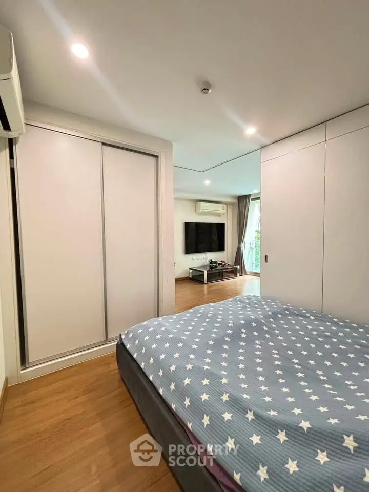 Spacious bedroom with modern decor and sliding closet doors, adjacent to a cozy living area.